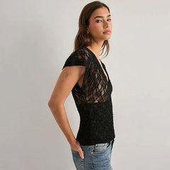 Woman wearing a black lace top and jeans on a plain background