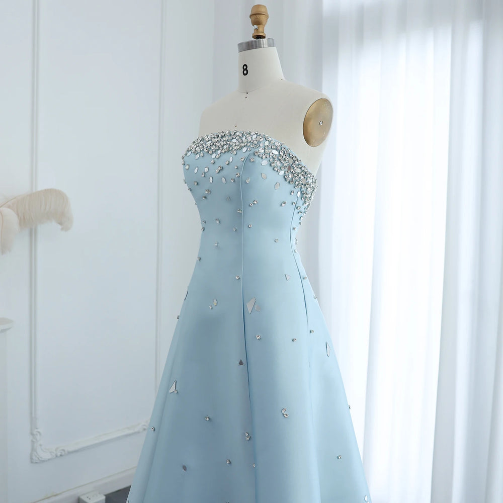 Light blue evening gown with bead embellishments on a mannequin against a white curtain background.