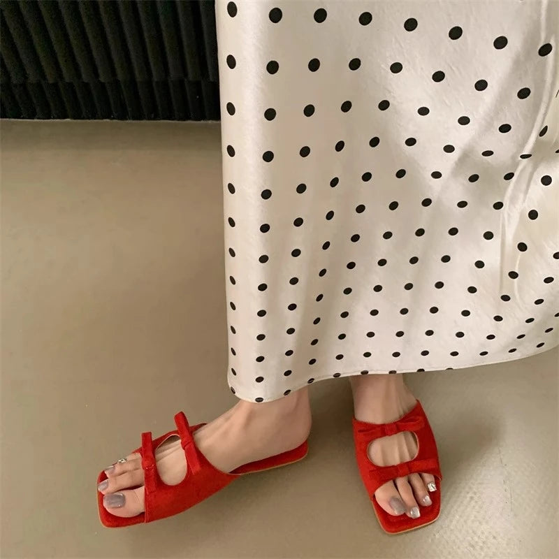 Red sandals worn with a white skirt featuring black polka dots on a neutral background