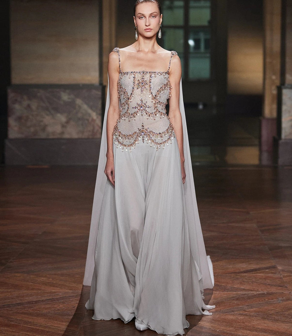 Model wearing a long, elegant dress with intricate detailing on a wooden floor.