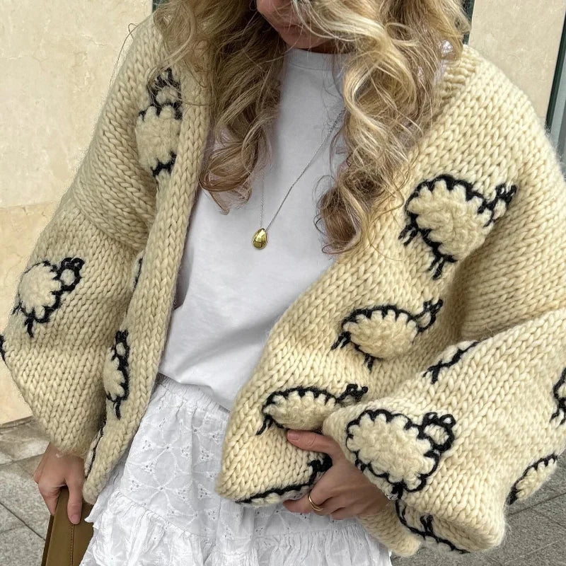 Person wearing a beige knitted cardigan with black sheep patterns.