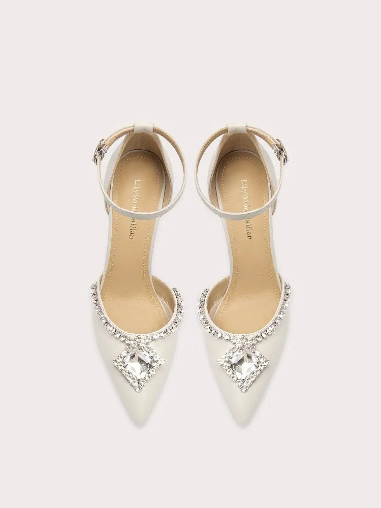 White high-heeled shoes with crystal embellishments on a light gray background