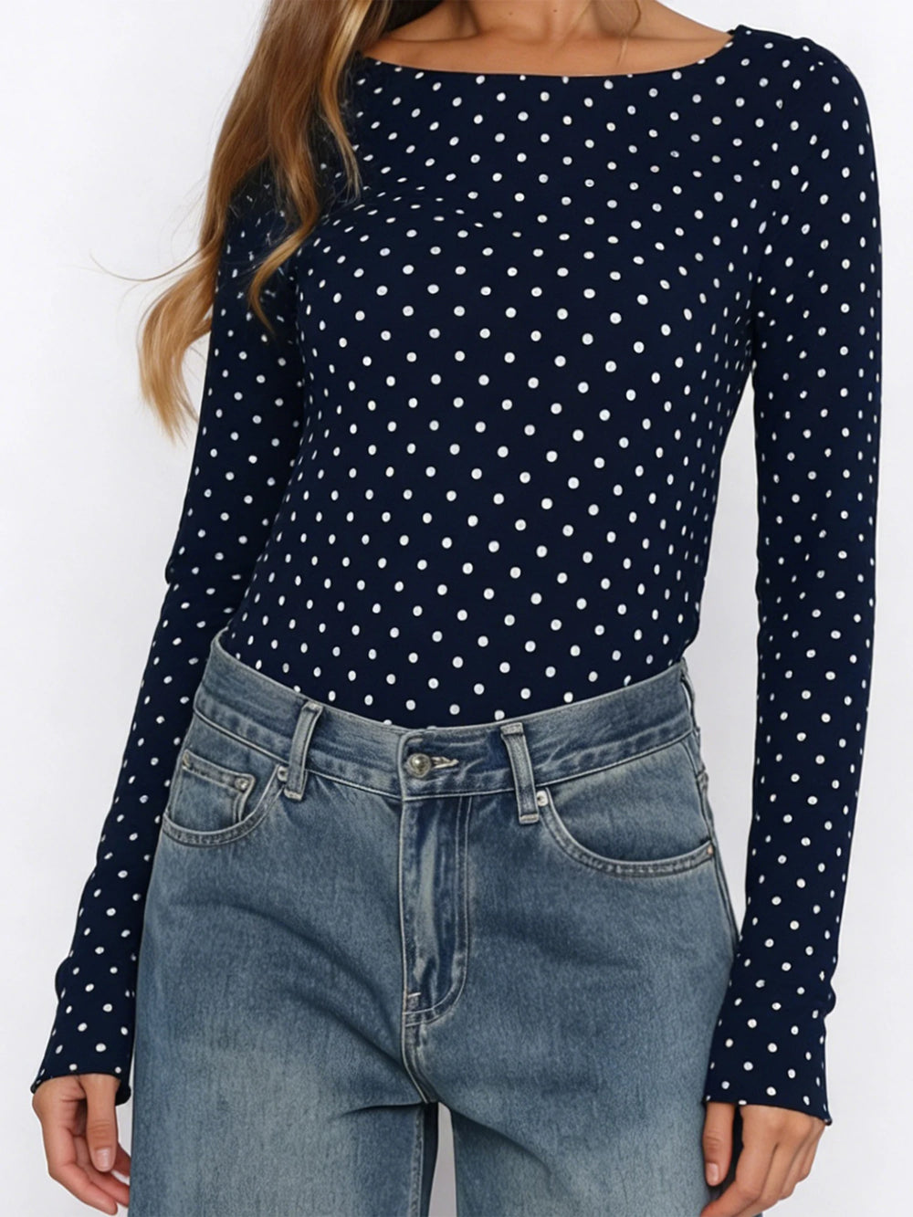 Person wearing a navy blue long-sleeve top with white polka dots and blue jeans on a white background