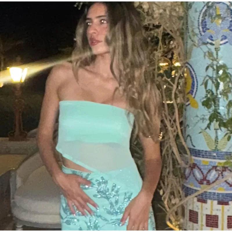 Woman in a light blue strapless top and skirt standing outdoors at night.