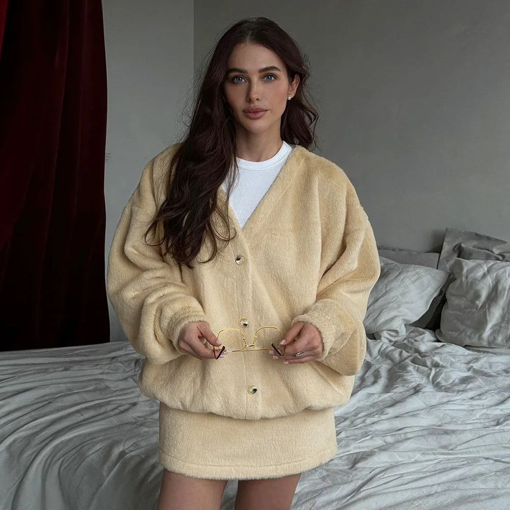 Woman wearing a beige cardigan over a white shirt in a bedroom setting.