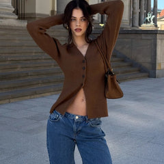 Woman wearing a brown cardigan and blue jeans standing in front of classical architecture.