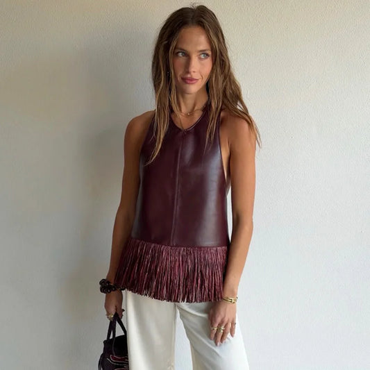 Woman wearing a burgundy leather top with fringe details against a plain background