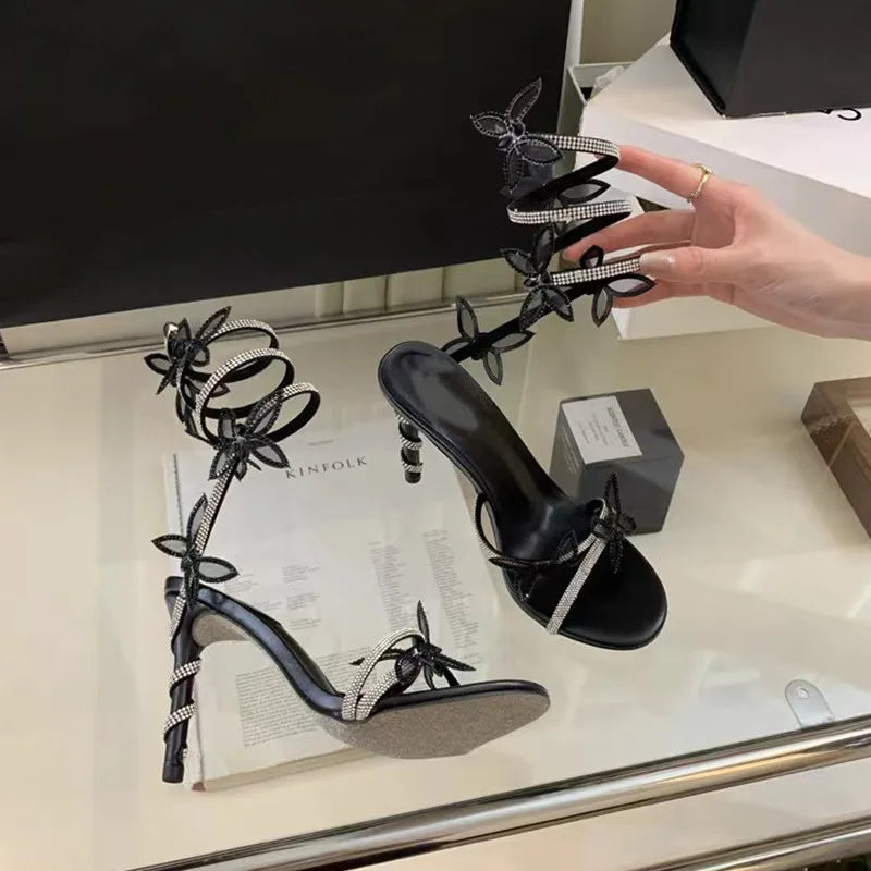 Black high-heeled shoes with floral designs on a glass surface.
