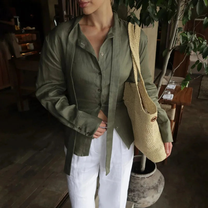 Person wearing a green shirt and white pants holding a beige woven bag indoors.