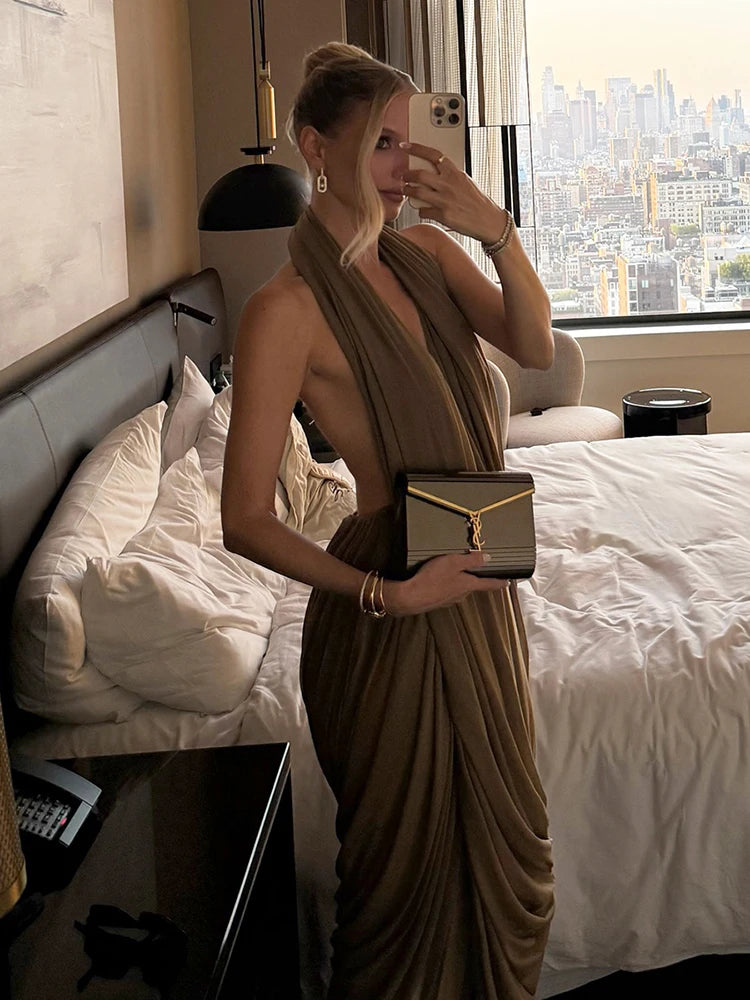 Woman in a brown dress holding a gold clutch in a room with a cityscape view.