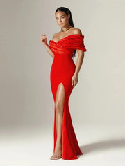 Woman wearing a red off-shoulder gown with a high slit on a plain background