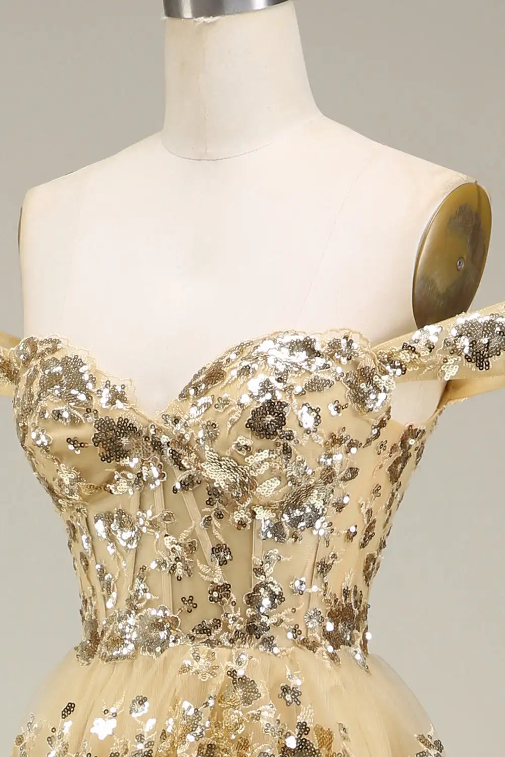 Mannequin wearing a beige evening gown with sequin embellishments on a plain background
