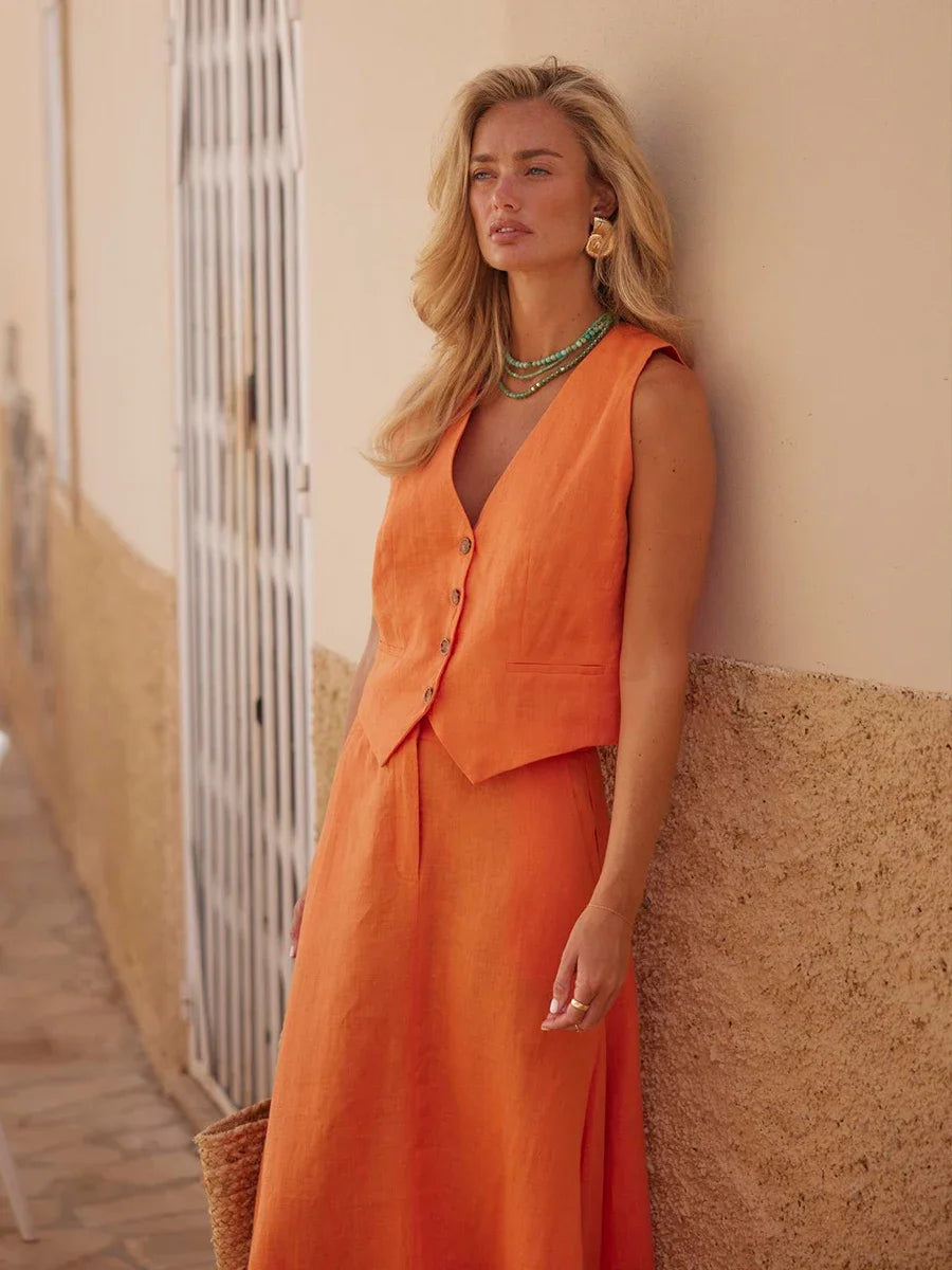 Woman in an orange dress leaning against a textured wall.