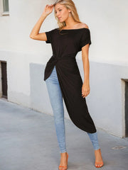 Woman wearing a black off-shoulder top and light blue jeans against a white wall.