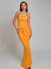Woman wearing a bright yellow outfit with a top and long skirt on a plain background