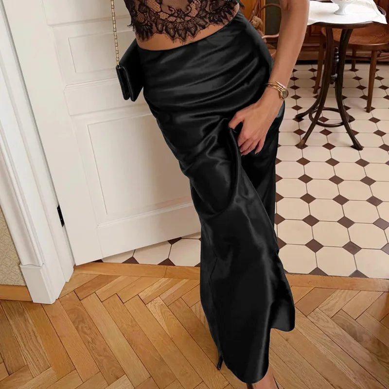 Person wearing a black satin skirt in an indoor setting with wooden flooring and a tiled wall.
