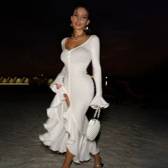 Woman in a white dress holding a handbag at night.