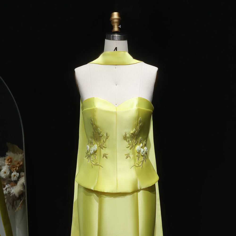 Yellow evening gown with floral embroidery on a mannequin against a black background