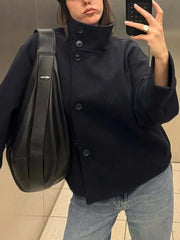Close-up of the high neck and button details on a black cropped jacket.