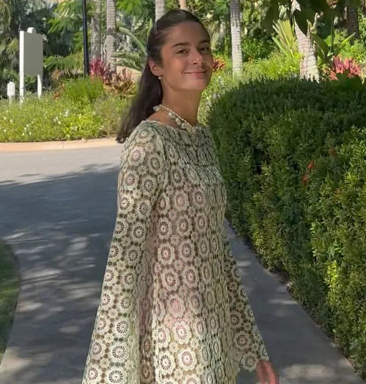 Woman in a patterned dress standing outdoors with greenery in the background