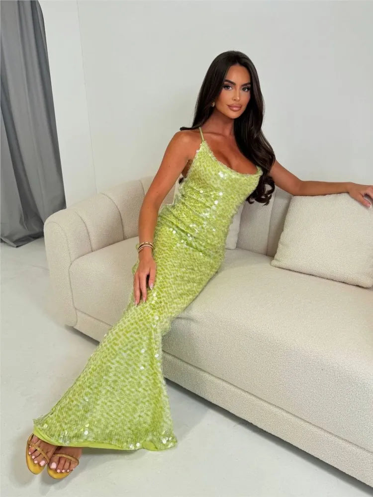 Woman in a green sequin dress sitting on a couch in a room.