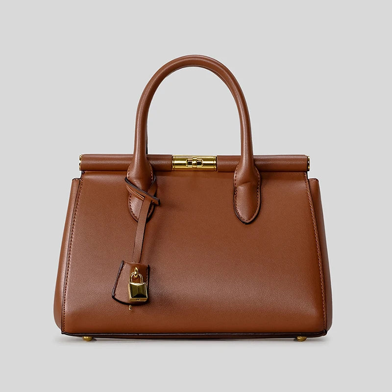 Brown structured top-handle satchel bag with gold clasp and lock detail against a grey background.