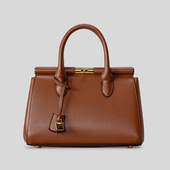 Brown structured top-handle satchel bag with gold clasp and lock detail against a grey background.