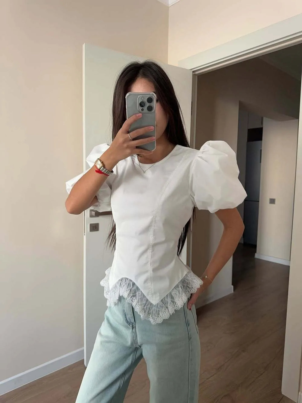 Person wearing a white blouse with puffed sleeves and light blue jeans in a room.