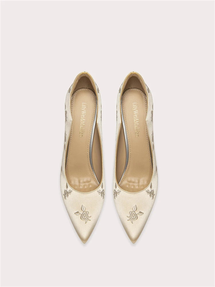 Pair of cream-colored pointed-toe shoes with floral patterns on a light gray background