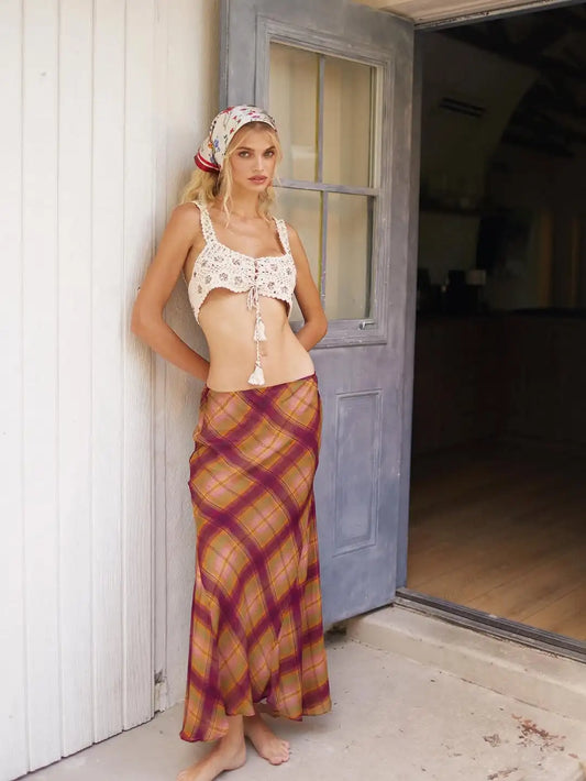 Woman leaning against a door wearing an irregular hem plaid maxi skirt and a crochet top.