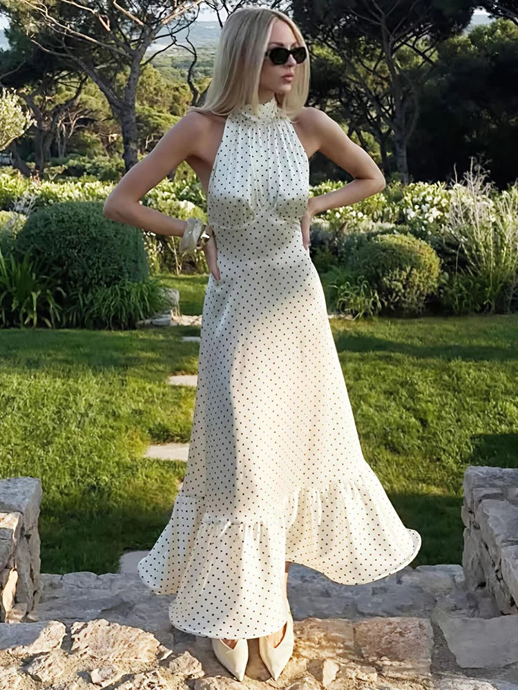 Woman in a white polka dot dress standing outdoors in a garden setting