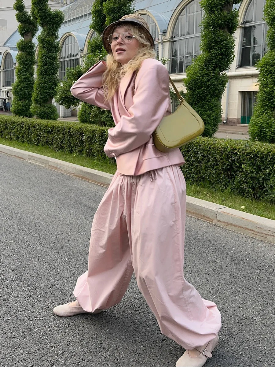 Person wearing a pink outfit with a beige bag on a street.