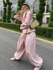 Person wearing a pink outfit with a beige bag on a street.