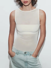 Person wearing a white sleeveless top and light blue jeans against a plain background