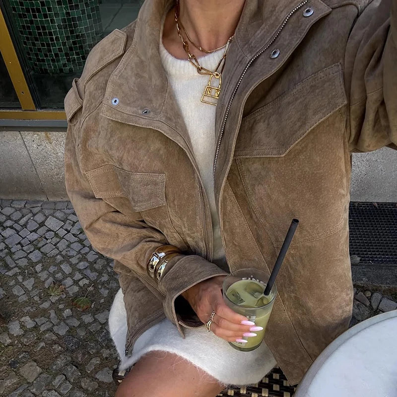 Person wearing a brown suede jacket holding a drink with a straw outdoors.