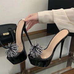 Hand holding a black platform stiletto mule with clear PVC and silver rhinestone embellishments