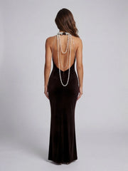 Woman wearing a black evening gown with a pearl necklace on a plain background