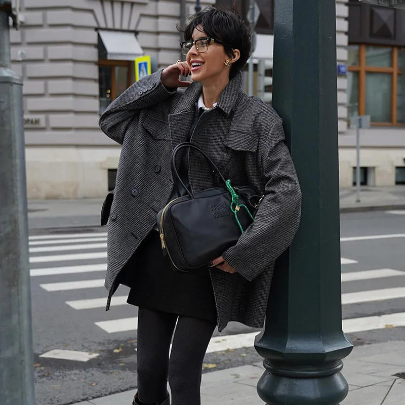 Woman in a gray coat leaning against a street lamp on a city street