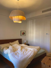 A modern designer fabric pendant light with a soft, warm glow hanging in a cozy bedroom. C