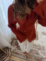 Person wearing a red blouse and white pants standing in a room with a mirror and patterned rug.