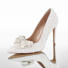 Side profile of a white pointed toe stiletto heel covered in pearls with a crystal bow