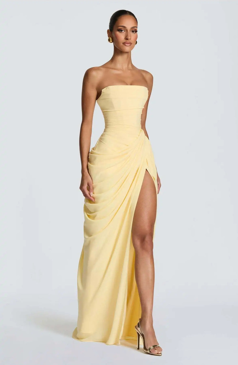 Woman wearing a strapless yellow evening gown with a slit on a white background