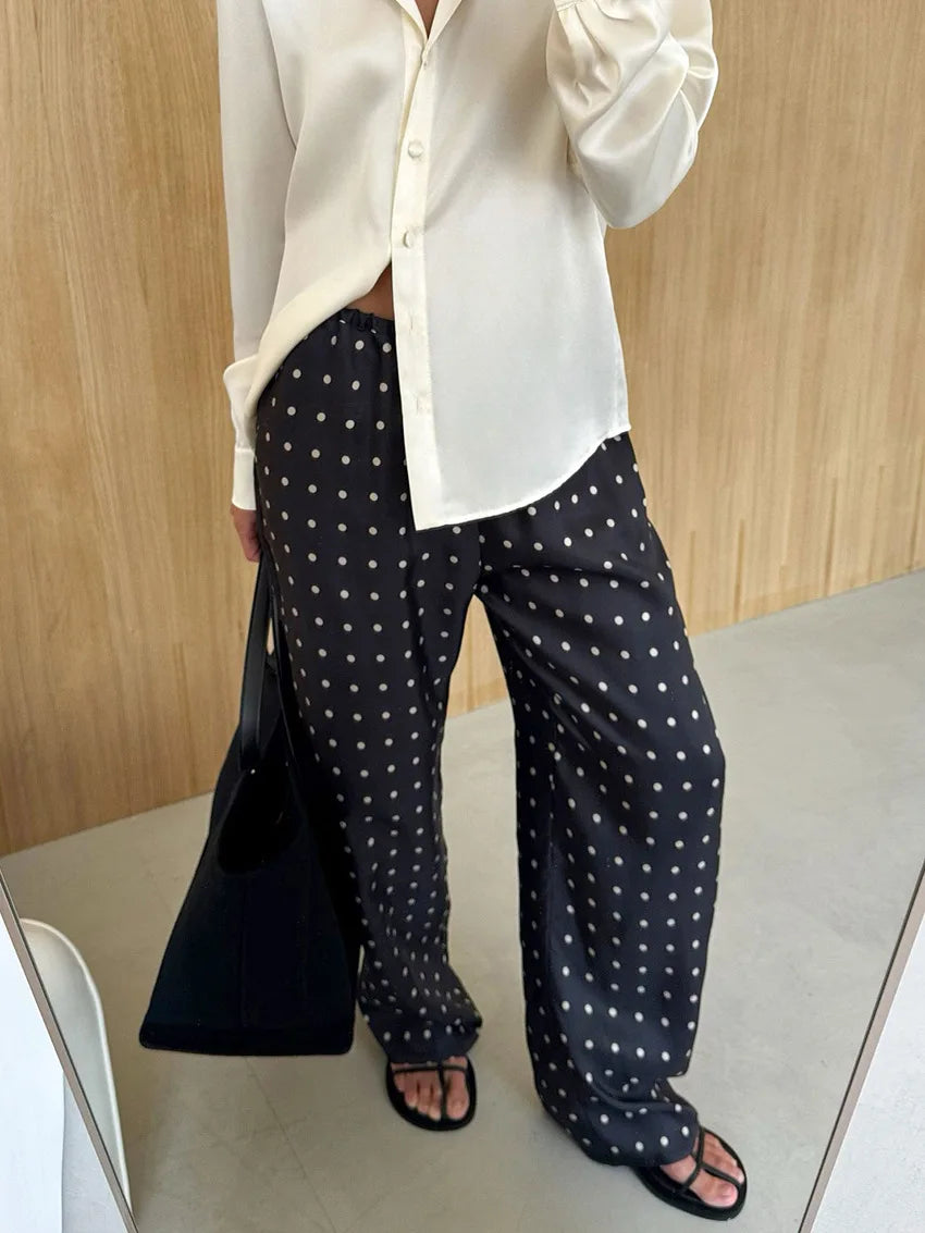 Person wearing a white shirt and black polka dot pants against a wooden wall.