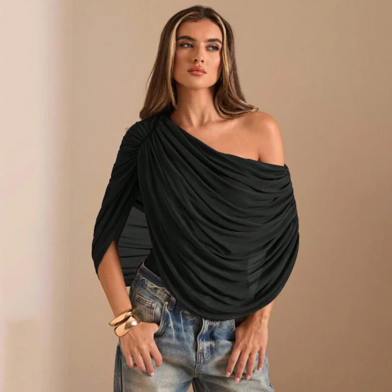 Woman wearing a black off-shoulder top and blue jeans against a beige background