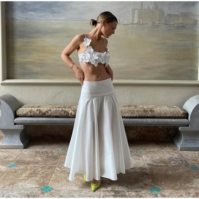Woman in a white floral top and skirt standing in a room with a large painting on the wall.