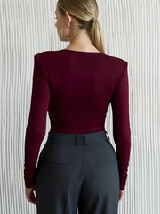 Person wearing a burgundy long-sleeve top and dark gray pants against a light gray background
