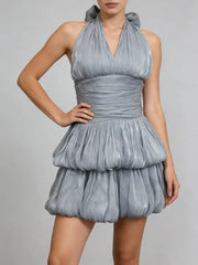 A woman wearing a blue pleated dress against a plain background