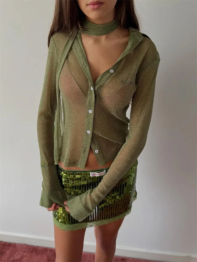 Person wearing a green sheer cardigan over a matching skirt with a white wall background
