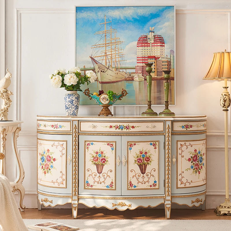 Decorative sideboard with floral patterns in a room with a painting of a ship and buildings.