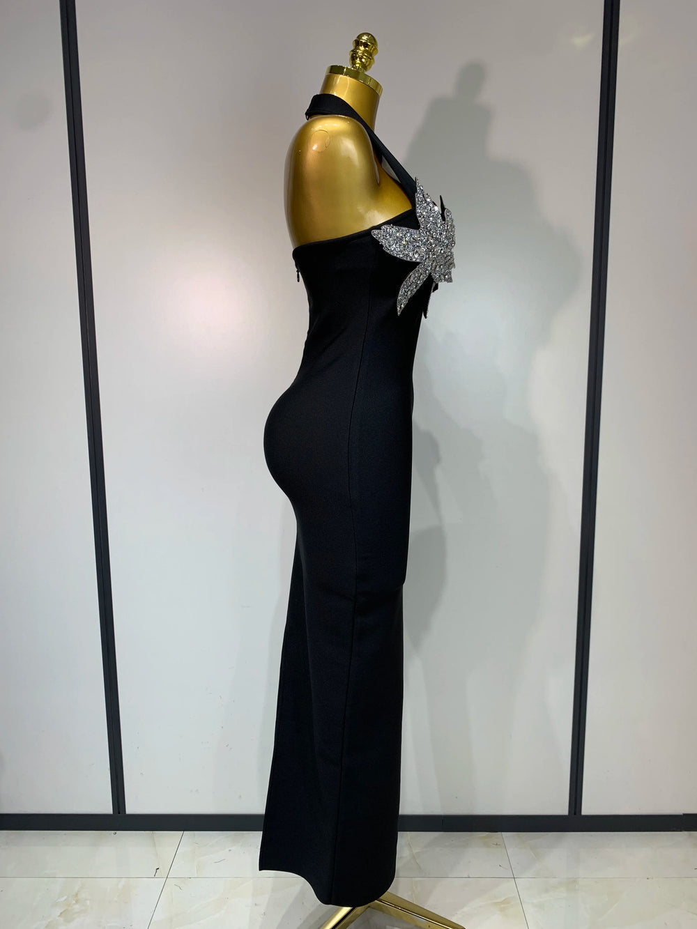 Black evening gown with a large bow on a mannequin against a white wall.